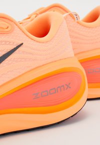 Detailaufnahme von Pfirsich- und Orangenen Nike-Laufschuhen mit ZoomX-Dämpfungsmittelsohlen und schwarzen Swoosh-Logos.