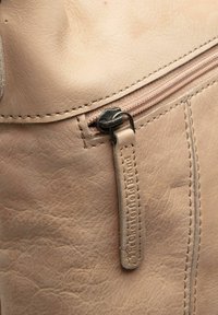 Sac en cuir beige clair avec une poche zippée dotée d'une languette, des coutures visibles et une petite étiquette de marque près de la fermeture éclair.