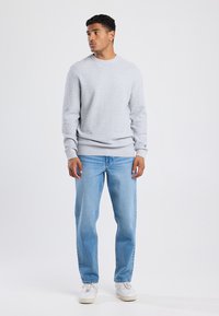 Gray textured sweater with a ribbed crew neckline, paired with light blue straight-leg jeans and white sneakers on a plain background.
