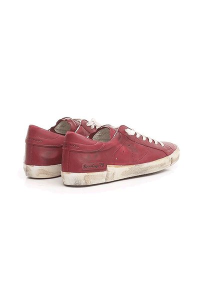 Baskets en cuir rouge avec des lacets blancs, bords usés et semelles éraflées. Présente un logo sur le côté et un design bas classique.