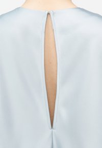 Άνω όψη πίσω μέρους ανοιχτόχρωμου μπλε ενδύματος με κατακόρυφο άνοιγμα που κλείνει με ένα μικρό γάντζο στο λαιμό.