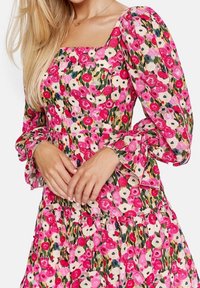 Florales Kleid mit puffärmel, das über einen quadratischen Ausschnitt verfügt. Das Material ist leicht und hat ein pinkes Blumenmuster auf einem cremefarbenen Hintergrund.