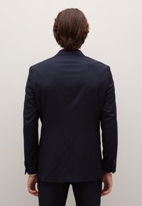 Donker marineblauw colbert met krijtstreeppatroon, enkellangs ontwerp en notched revers. Heeft knoopmanchetten en een op maat gemaakte pasvorm.