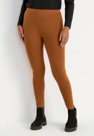 Braune Leggings aus dehnbarem Stoff mit hoher Taille und glatter Textur, kombiniert mit schwarzen Stiefeletten.