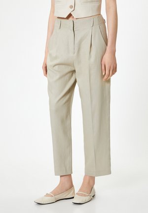 Light beige linen trousers with a relaxed fit, pleats at the front, and side pockets, paired with cream ballet flats featuring a strap.