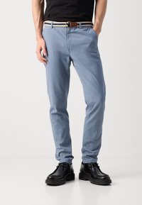 Svijetloplave chinos hlače od pamuka, sa slim fit krojem i standardnim džepovima, uparene s višebojnim pojasom i crnim cipelama.