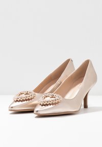 Metallic gold high heel shoes with pointed toes, featuring decorative crystal embellishments at the front and a smooth satin-like texture.