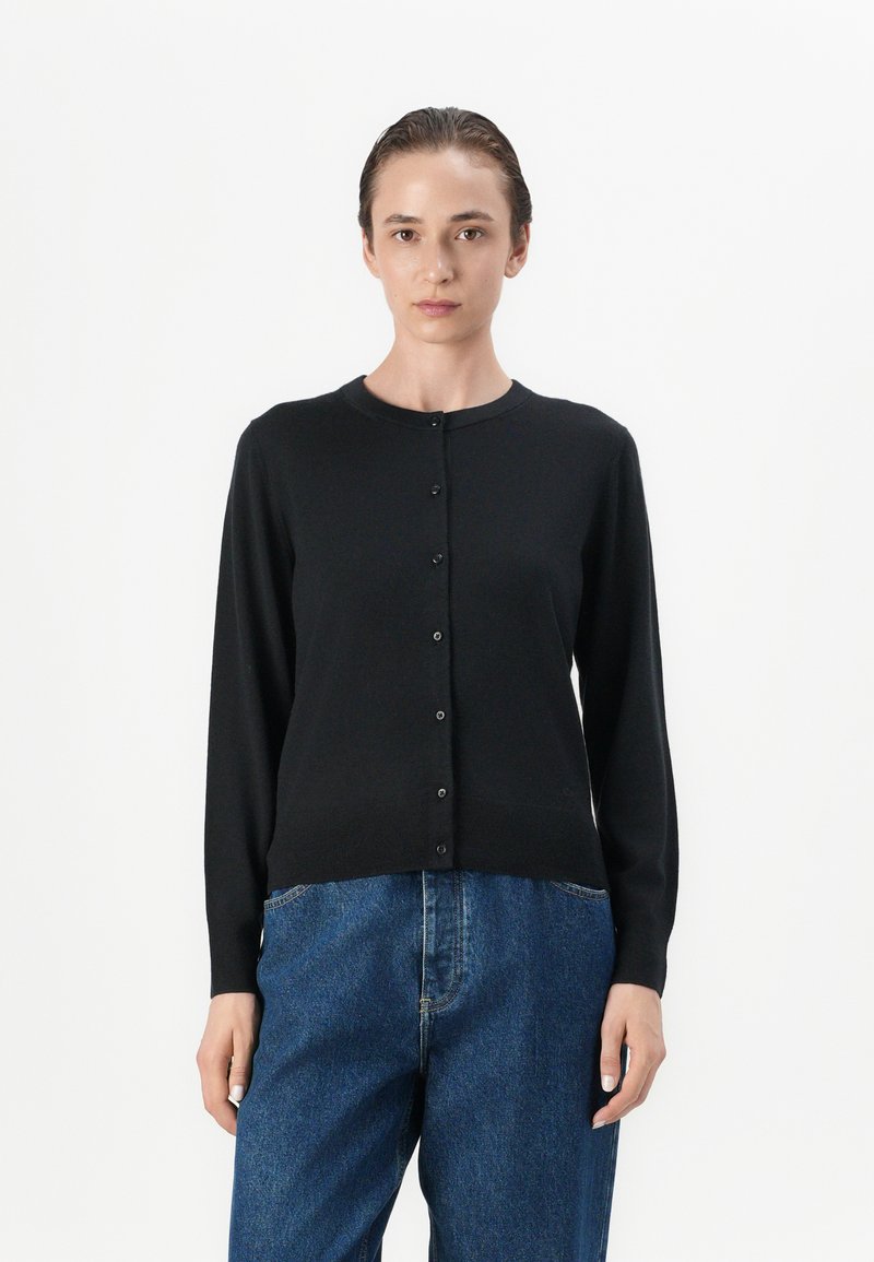 Cardigan lungo nero a maniche lunghe realizzato in un tessuto a maglia liscia, con scollatura tonda e chiusura con bottoni sul davanti. Abbinate a jeans blu.