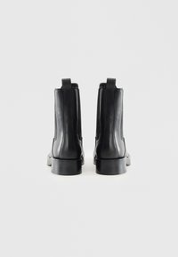 Botas de cuero negras hasta el tobillo con un acabado liso, paneles elásticos en los lados y lengüetas en la parte trasera. Diseño de puntera cuadrada y tacón bajo tipo bloque.