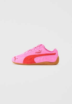 Baskets Puma roses et rouges avec semelle en gomme, logo latéral et lacets, présentées sur un fond gris clair uni.