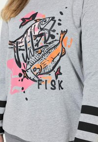 Grijze sweatshirt met een gedurfde visafbeelding in oranje en zwart, met roze spatten en zwart gestreepte accenten op de mouwen.