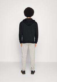 Sweat à capuche noir avec une coupe décontractée et des poignets côtelés, associé à un pantalon de jogging gris clair. Des baskets noires complètent la tenue.