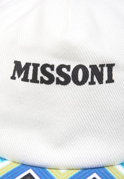 Cappello bianco con logo "MISSONI" nero. La visiera presenta un motivo geometrico colorato in blu, giallo e nero. Texture morbida evidente.