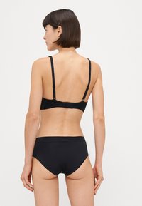Crni bralet s podesivim trakama i kopčanjem na kukicu; uparen s matching crnim bikinijem nalik donjem dijelu s glatkom, rastezljivom teksturom.