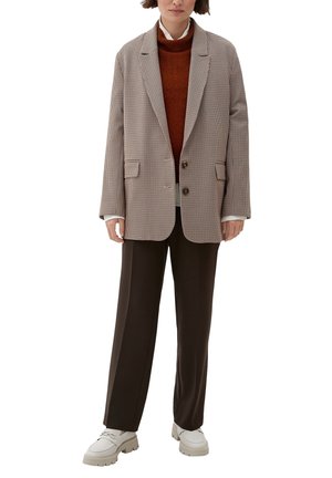 Blazer à carreaux en beige et marron, coupe oversize, avec deux boutons, associé à un turtleneck marron et un pantalon marron foncé, terminé par des bottes blanches.