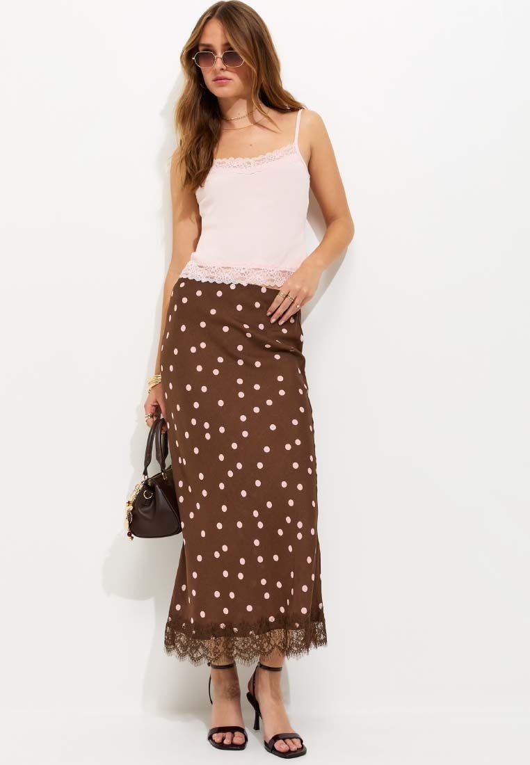 Woman wearing a pink lace-trimmed cami, brown polka dot midi skirt with lace hem, black heeled sandals, sunglasses, and holding a brown handbag.