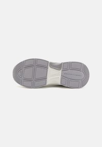 Suela de zapatilla con una superficie de goma gris texturizada, que presenta un patrón geométrico y un logo, y una entresuela blanca para mayor estabilidad y amortiguación.