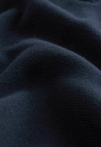 Dunkelblauer gestrickter Stoff mit einem strukturierten Muster, das eine weiche und leicht erhabene Oberfläche aufweist und ein warmes Erscheinungsbild erzeugt.