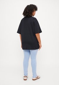 Svart oversized t-skjorte laget av bomull, med korte ermer og avslappet passform, sammen med lyseblå smal jeans og beige sneakers.
