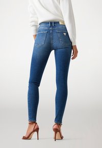 Svetlo modri skinny traper hlače z gladko teksturo, srednje visoko pasom, dvema zadnjima žepoma in rahlim zbledelostjo. Nosi se z rjavimi salonarji.
