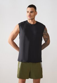 Juodas be rankovių marškinėlis, pagamintas iš minkštos medžiagos, su apvaliu kaklu ir laisvu siluetu. Derinamas su žaliais šortais su balta apdaila.