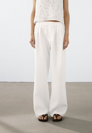 White linen wide-leg trousers with front pleats, paired with black flip-flops. Lightweight fabric and relaxed fit enhance comfort.