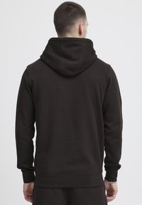 Sweatshirt à capuche marron en tissu doux, avec une coupe décontractée, des manches longues et des poignets et un ourlet côtelés. Design monochrome.