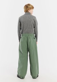 Groene, waterdichte broek met een losse pasvorm en een elastische tailleband, gecombineerd met een grijs langemouwtop, gezien vanaf de achterkant.