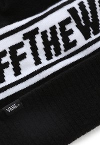 Gorro de punto negro con una banda blanca que muestra el texto "OFF THE WALL" en una fuente en negrita. Presenta una pequeña etiqueta negra de Vans.