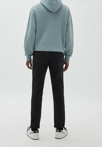 Světlá modrá mikina s kapucí, pohled zezadu, v kombinaci s tmavými kalhotami a bílými teniskami s černými prvky. Měkká textura, ležérní design.