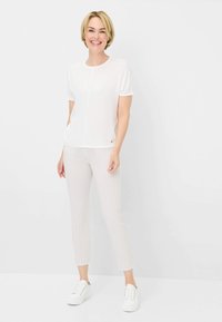 Weißes Kurzarmoberteil mit Rundhalsausschnitt, kombiniert mit hell gestreiften, taillierten Hosen und weißen Sneakers, vor einem neutralen Hintergrund.