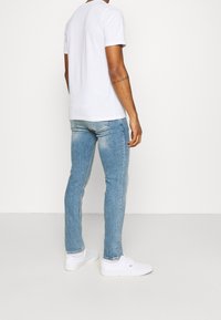 Bílé bavlněné tričko s kulatým výstřihem, spojené s světle modrými džínami. Outfit doplňují bílé plátěné tenisky.