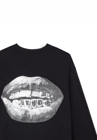 Schwarzer Kapuzenpullover mit einem großen Grafikdesign von glänzenden Lippen mit goldenen Zahnschienen, das ein auffälliges, metallisches Design hervorhebt.