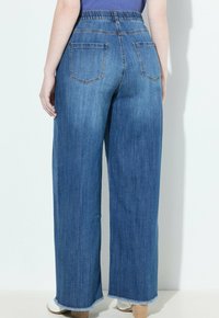 Jeans de mezclilla azul de pierna ancha con una cinturilla elástica alta, dos bolsillos traseros y detalles de dobladillo sin hacer en los tobillos. Textura suave.