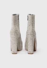 Botas de tobillo plateadas con tacones altos y gruesos, completamente cubiertas de brillantes rhinestones y cremalleras laterales, mostradas desde la parte posterior.