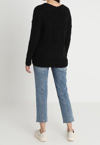 Pull noir en peluche fabriqué à partir d'un tissu texturé, présentant une coupe décontractée, un col rond et des manches longues, associé à un jean droit bleu clair.