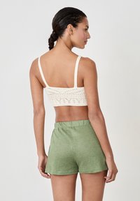 Bralette de ganchillo en blanco roto con tirantes finos, combinado con pantalones cortos de tiro alto en verde claro con cordón. Presenta un patrón de tejido abierto y un ajuste relajado.