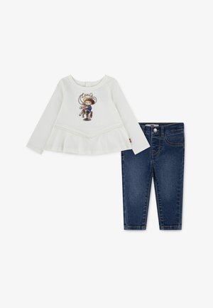 Camisola branca de manga longa com gráfico de cowboy e rendas; combinada com jeans de denim azul-escuro com fecho frontal e corte skinny.