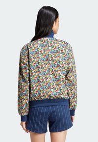 Floral bomber jacket featuring a multi-color pattern on a dark background, ribbed cuffs and hem, and a high collar. Paired with navy shorts.