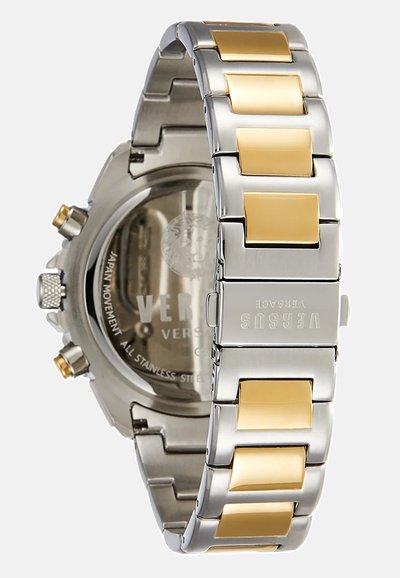 Montre en métal avec un bracelet en acier inoxydable et des accents dorés. Le boîtier a un fond transparent et des détails gravés.