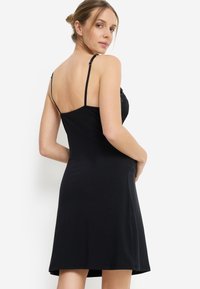 Μαύρο φόρεμα χωρίς μανίκια με στενή μπούστα και φουσκωτή φούστα. Διαθέτει λεπτές τιράντες και απαλό, ελαστικό ύφασμα για άνεση.