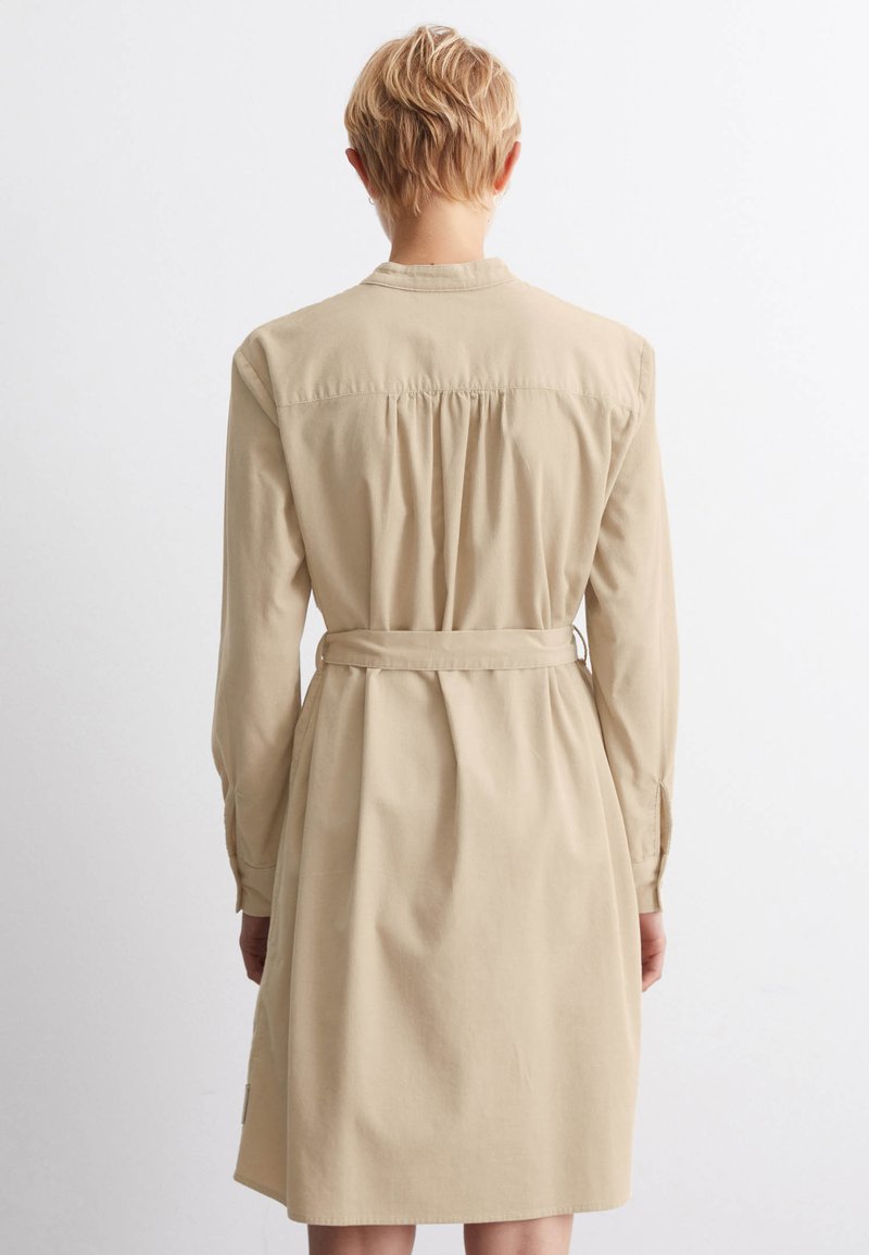 Beiges, langärmliges Kleid mit gerafftem Rücken, kragenähnlichem Hals und tailliertem Bund. Glatte, baumwollartige Textur, knielang mit leichtem A-Linien-Schnitt.