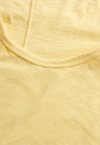 Tela de algodón amarilla con una textura suave, cuello redondo y detalles de costura visibles. Color uniforme con un ligero efecto jaspeado.