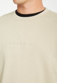 Beige crewneck sweatshirt made of soft fabric, featuring an embroidered "VOLCOM" logo on the chest and a black inner neckline.
