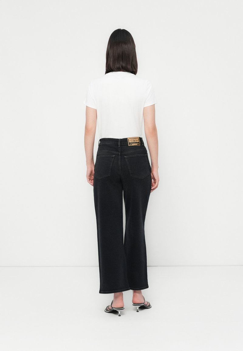Jean large noir à taille haute avec poches arrière, associé à un t-shirt blanc uni. Patte en cuir sur la taille. Texture lisse.