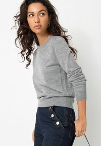 Grå crew-neck sweater i et blødt, struktureret strik med ribbetrukne ærmer og kant, parret med mørkeblå højttlivede jeans med guldknapper.