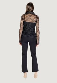 Blusa di pizzo nero con maniche lunghe e motivo floreale, dotata di colletto. Abbinata a pantaloni neri aderenti e tacchi nudi.