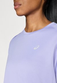 Kerge lilla sportlik särk, millel on ümar kaelus, lühikesed varrukad ja diskreetne logo vasakul küljel. Valmistatud siledast, hingavast kangast.