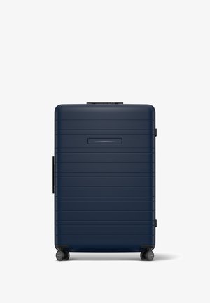 Valise rigide de couleur marine avec des rainures horizontales, une poignée rétractable et quatre roues. Dispose d'un emplacement pour une carte d'identité mince à l'avant.