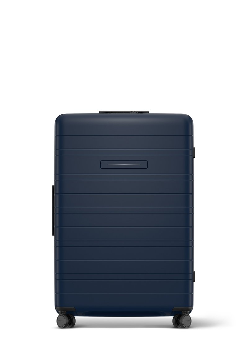 Valise rigide de couleur marine avec des rainures horizontales, une poignée rétractable et quatre roues. Dispose d'un emplacement pour une carte d'identité mince à l'avant.